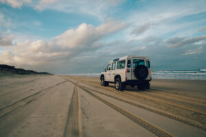 Weißer Geländewagen auf dem Sandstrand von K’gari neben dem Meer